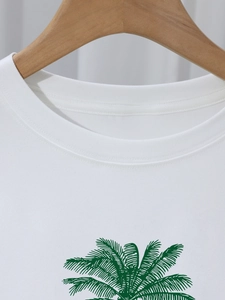 Minimalist white crew neck cotton T-shirt featuring a green coconut tree print on a hanger