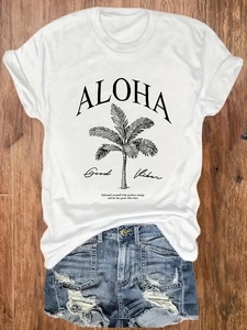 Women's white graphic T-shirt with palm tree print and denim shorts on wood background