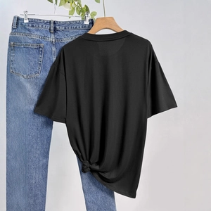 Détail d'un t-shirt noir à col rond avec nœud latéral et jean bleu délavé classique