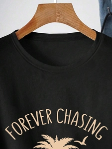 Detail of black cotton T-shirt featuring beige FOREVER CHASING text and palm tree print