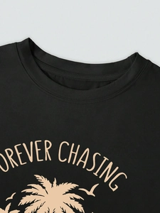 Detail of crew neck ribbing and Forever Chasing tropical print on black cotton T-shirt