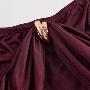 Detail of burgundy V-neck dress featuring a stylish gold metal ring accent on pleated fabric