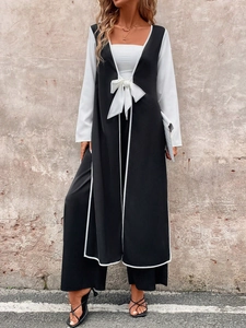 Detail view of a black long tie-waist vest with white trim over a white long-sleeve shirt