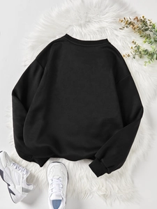 Vue arrière d'un sweat-shirt noir à col rond sur fond pelucheux avec baskets et plantes