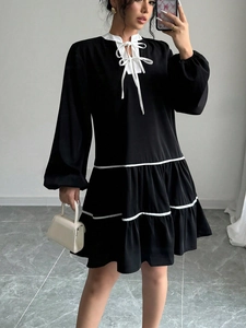 Detail of long-sleeved black dress with tiered skirt, white bow tie, and ruffled collar