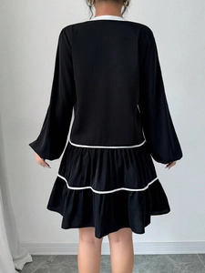 Rear view of a black tiered dress featuring contrasting white lines and long sleeves