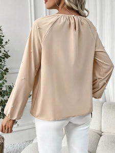 Detail of elegant apricot blouse featuring pearl-embellished sleeves and back keyhole closure