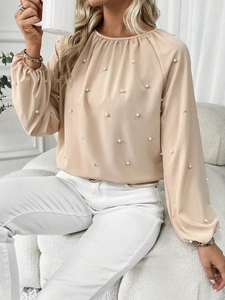 Detail of elegant beige long-sleeve blouse with white pearl embellishments and round neck