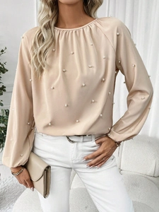 Detail of elegant beige chiffon blouse featuring pleated neckline and delicate pearl accents