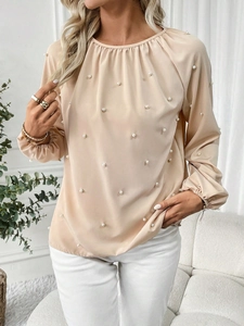 Detail of elegant apricot satin blouse featuring delicate pearl beads and pleated neckline