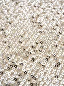 Macro shot of silver sequins stitched on beige mesh fabric for a shiny metallic texture