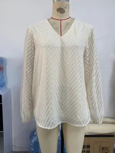 Détail de la blouse blanche à col en V montrant le motif à chevrons et les poignets élastiques