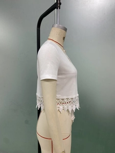 Close-up of white knitted crop top showing intricate floral crochet lace hem detail