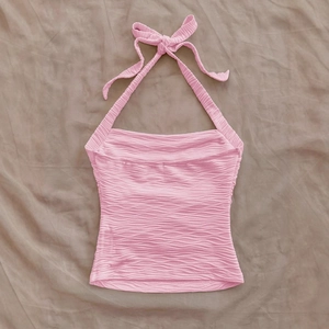 Pink halter top with wavy textured fabric and neck tie bow shown on gray background