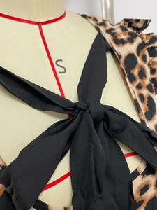 Detail of leopard print dress featuring black bow shoulder ties on a textured fabric