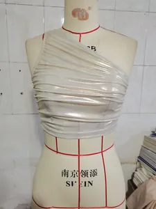 Dettaglio del crop top bianco lucido monospalla con pieghe orizzontali su manichino
