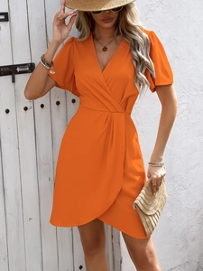 Close-up of bright orange V-neck wrap dress with cinched waist and pleated skirt detail