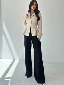 Dettaglio del blazer beige sfiancato con pieghe e pantaloni neri a gamba larga