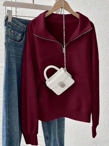 Detail of burgundy oversized half-zip sweatshirt with ribbed cuffs and white mini bag