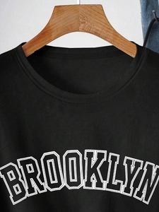 Close-up of black cotton t-shirt featuring white Brooklyn collegiate print on wooden hanger
