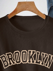 Detail of Brooklyn print on dark brown cotton t-shirt hanging on a wooden hanger