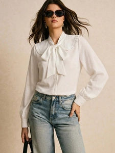 Detail of white long sleeve blouse featuring ruffled Peter Pan collar and bow neck tie