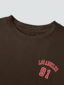 Detail des Los Angeles Aufdrucks auf braunem Baumwoll-T-Shirt mit Rundhalsausschnitt