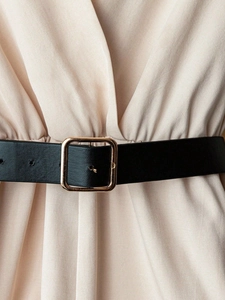 Elegant women black leather belt with golden square buckle on a creamy beige dress