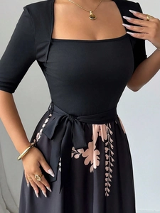Dettaglio dell'elegante abito nero con scollo quadrato, stampe floreali e cintura a fiocco