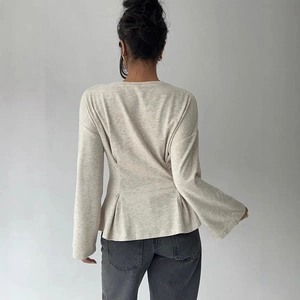 Oatmeal knit long sleeve top with flared cuffs and peplum waist on grey denim