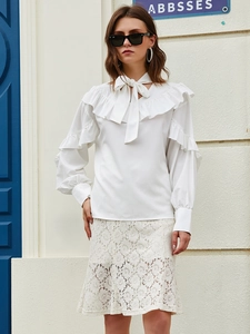 Close-up of a white long-sleeve blouse featuring tiered ruffles and V-neck tie detail