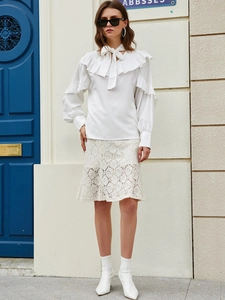 Detail of white long sleeve blouse featuring ruffled shoulders and tie-neck bow design