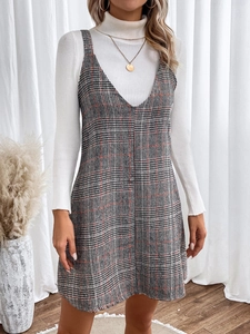 Detail of V-neck plaid strap dress layered with ribbed white turtleneck sweater