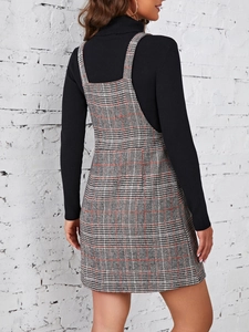 Détail de la robe chasuble à carreaux gris portée sur un pull à col roulé noir chic