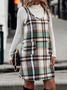 Detail des karierten Trägerkleids mit großen Taschen und weißem Rollkragenpullover