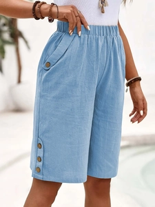 Detail of light blue linen shorts featuring decorative wooden buttons on the leg hem