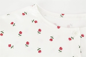 Gros plan sur une maille côtelée blanche à imprimé floral rouge et petit bouton blanc