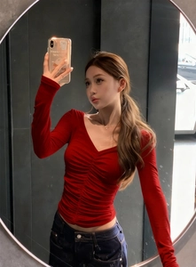 Detail of ruched red long sleeve top with deep V-neck and slim fit texture