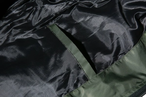 Detailed macro view of dark green bomber jacket showing smooth black inner lining and pocket