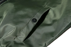 Close-up of olive green bomber jacket featuring nylon satin fabric and snap button pocket