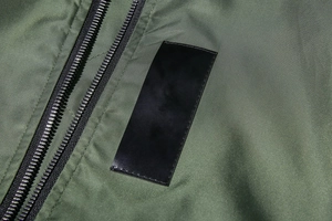 Detail of military green MA1 bomber jacket featuring double black zippers and fabric texture