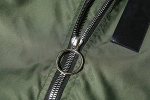 Macro shot of silver circular metal zipper puller on army green bomber jacket fabric