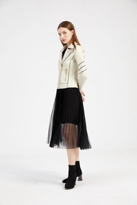Full body view of women's cream faux leather jacket paired with black pleated tulle skirt