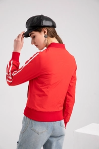 Detail view of red bomber jacket featuring white sleeve stripes and ribbed cuffs on model