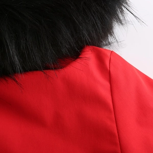 Détail de la parka d'hiver rouge montrant le col en fausse fourrure noire et la couture
