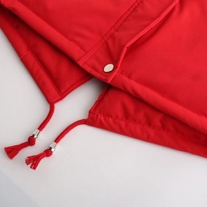 Détail de parka rouge avec cordon de serrage tissé, embouts argentés et bouton-pression