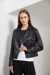 Détail d'une veste en similicuir noir avec fermetures éclair argentées et laçage aux manches