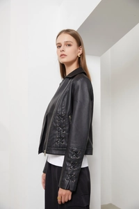 Détail d'une veste en similicuir noir avec poignets à lacets et fermetures éclair en métal