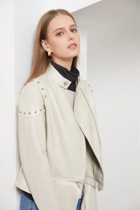 Detailed view of silver rivets on the shoulder of an off-white faux leather jacket