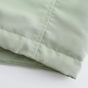 Détail macro du tissu parka vert clair montrant la texture sergée et la couture nette